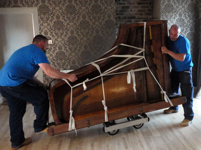 two movers moving a grand piano out of a house